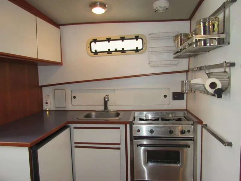 Slide: The Image of Compact kitchen in a 1997 Norstar 302 boat, featuring stove, sink, and storage shelves. - 32