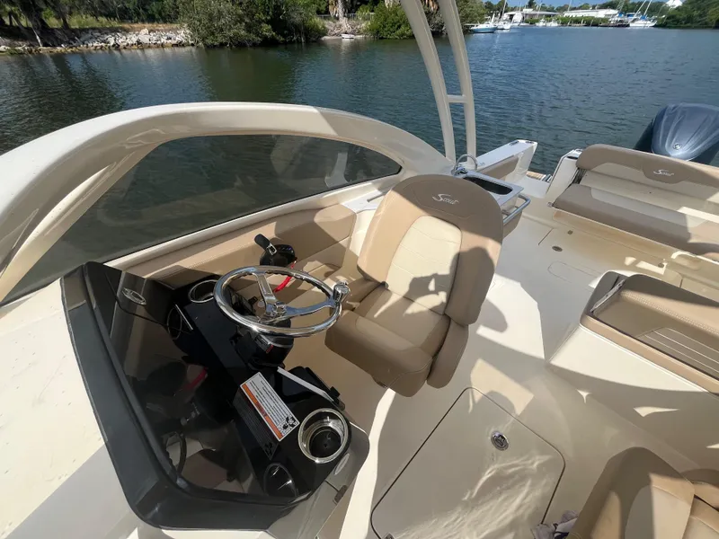 Slide: The Image of 2024 Scout 240 Dorado boat interior with steering wheel and seating, docked by the water. - 12