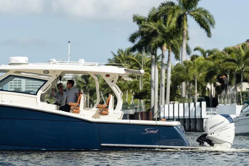 Slide: The Image of 2020 Scout 420 LXF boat cruising on water with palm trees in the background. - 2
