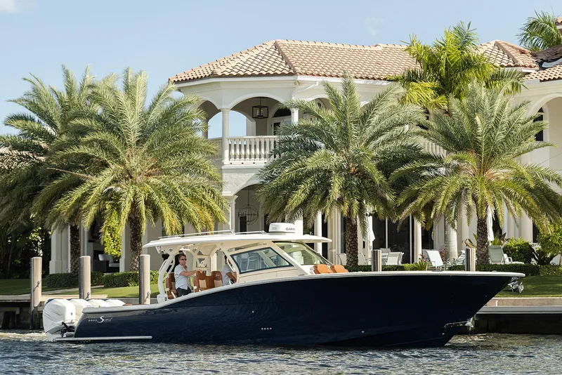 Slide: The Image of 2020 Scout 420 LXF boat docked near a luxurious waterfront mansion with palm trees. - 8