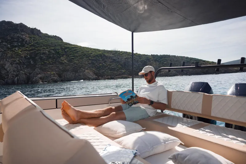 Slide: The Image of Man relaxing on Zodiac X10CC boat, reading under canopy, coastal backdrop. - 15