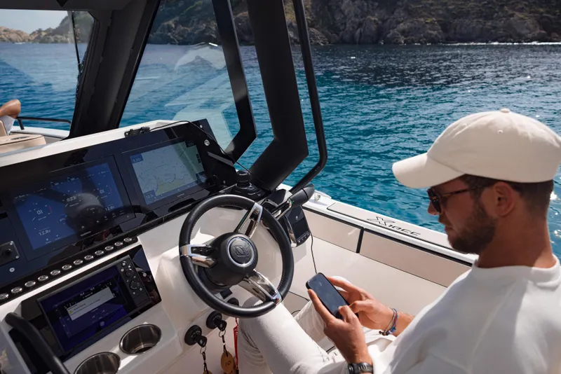 Slide: The Image of Man using phone on Zodiac X10CC boat, 2025 model, with scenic ocean view. - 4