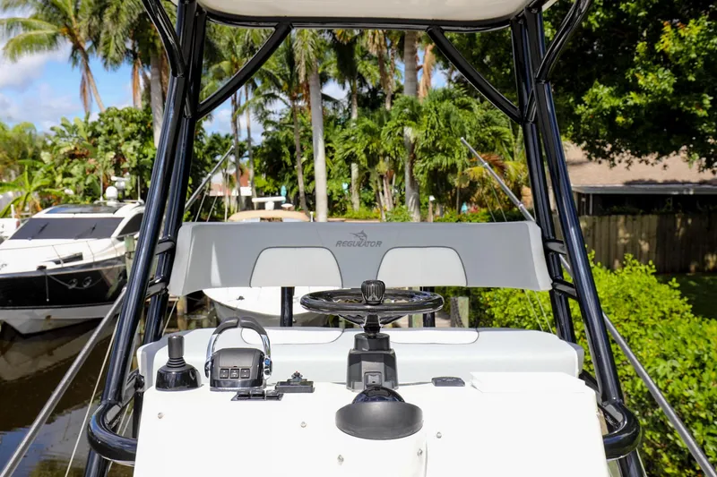 Slide: The Image of 2020 Regulator 41 boat helm with steering wheel and controls, docked near lush greenery. - 39