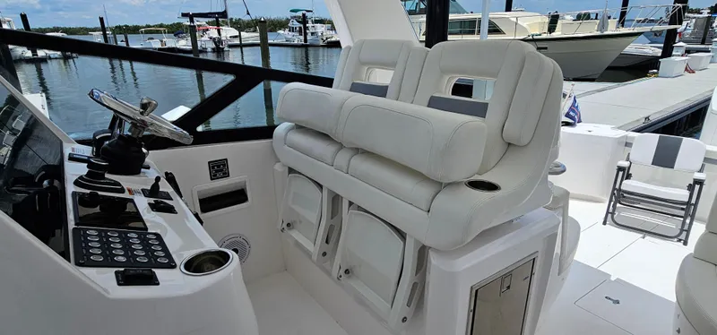 Slide: The Image of 2022 Intrepid 438 Evolution yacht helm station with plush seating at marina. - 11