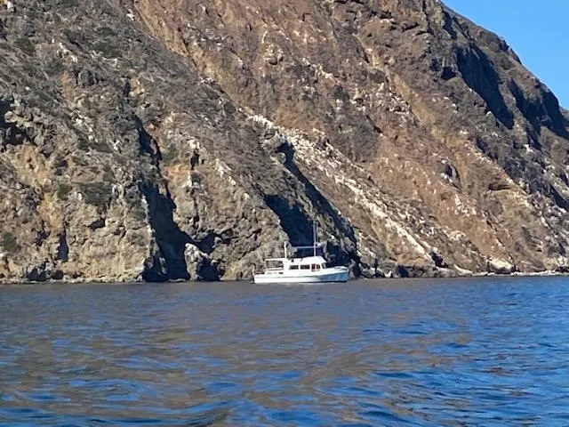 Slide: The Image of Grand Banks 42 Classic yacht near rocky coastline, 1969 model, on calm blue water. - 40