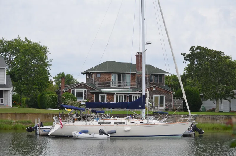 The Image of 1987 Sabre 42 sailboat docked near a house, with lush greenery in the background. - 1
