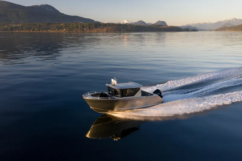 Slide: The Image of 2025 Jasper Marine Defender 22 boat cruising on a serene lake with mountain backdrop. - 11