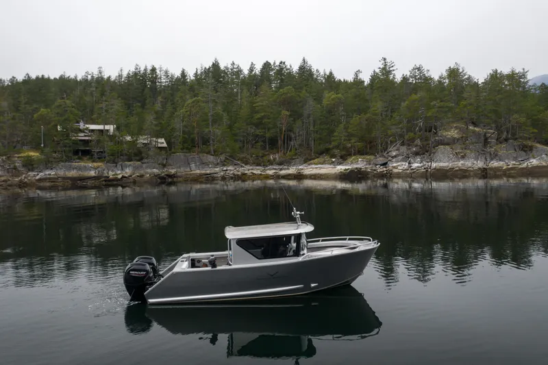 Slide: The Image of 2025 Jasper Marine Defender 22 boat cruising on a calm lake near a forested shoreline. - 9
