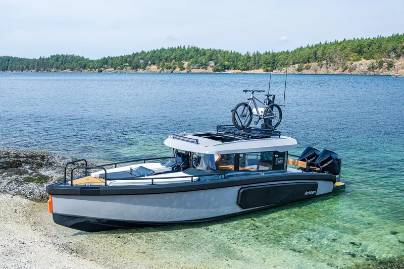 Slide: The Image of 2025 Arksen 30 boat docked on a scenic shoreline with a bicycle on the roof. - 0