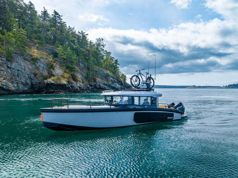 Slide: The Image of Arksen 30 boat cruising near a rocky shoreline, 2025 model, with bicycles on the roof. - 12