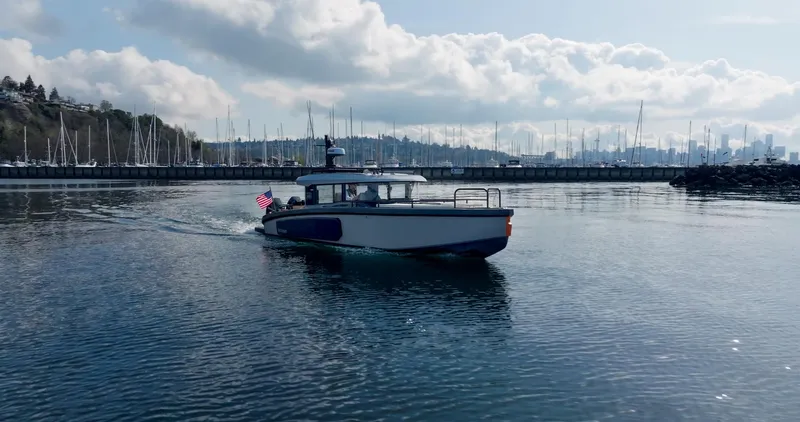 Slide: The Image of Arksen 30 boat cruising in a marina, 2025 model, with city skyline and cloudy sky. - 15