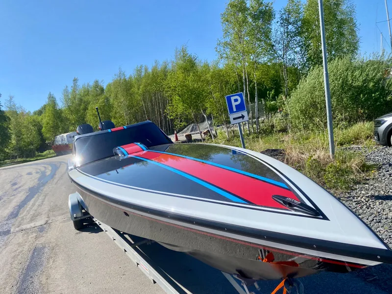 Slide: The Image of 2024 Nitra Boats 30 SkyTop on trailer, vibrant red and blue accents, parked near trees. - 10