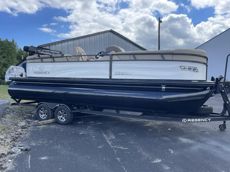 Slide: The Image of 2024 Regency 230 DL3 pontoon boat on a trailer, parked outdoors. - 0