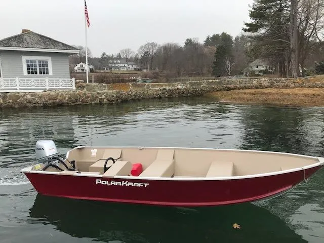 Slide: The Image of 2024 Polar Kraft Dakota 1670L boat on a calm lake near a house and flagpole. - 4