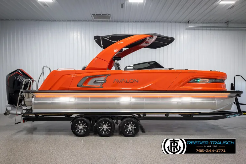 Slide: The Image of 2024 Avalon Excalibur VRB pontoon boat in vibrant orange, displayed indoors on a trailer. - 5