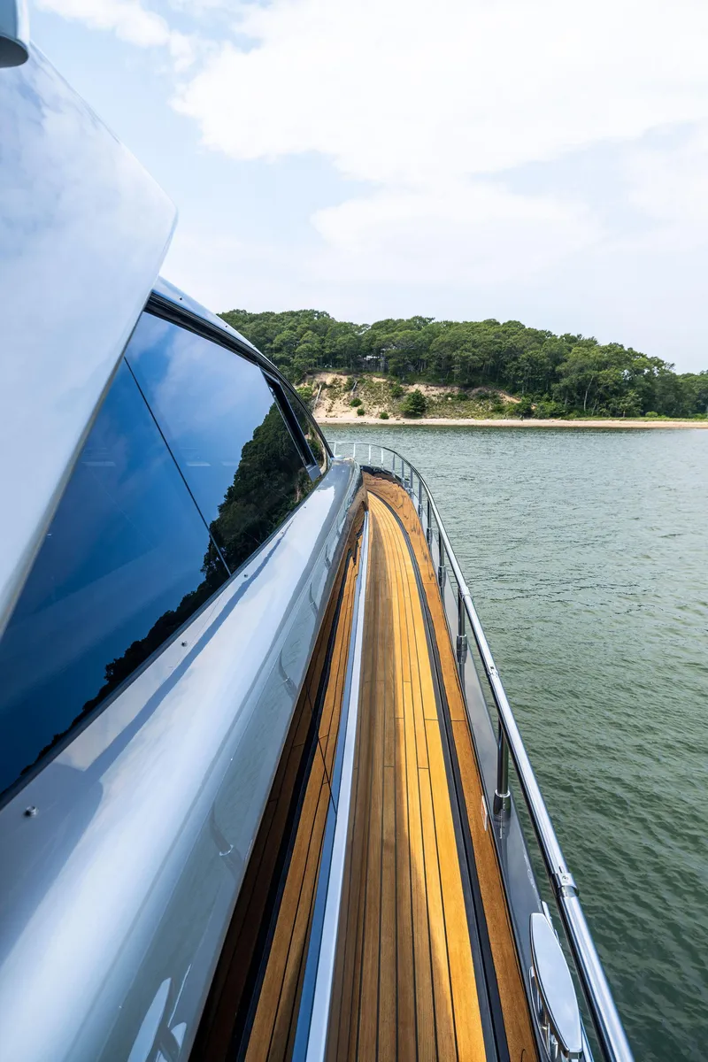 Slide: The Image of Side deck view of 2016 Riva 88' Domino Super yacht cruising near a forested shoreline. - 19