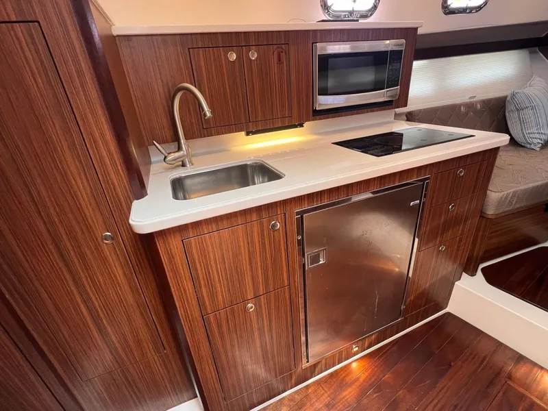 Slide: The Image of 2017 Pursuit OS 355 Offshore yacht kitchen with sink, microwave, and wooden cabinetry. - 26