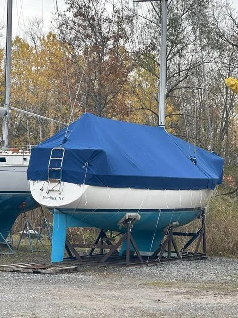 Slide: The Image of 1985 Pearson 36-2 sailboat with blue cover, stored on land, autumn trees in background. - 32