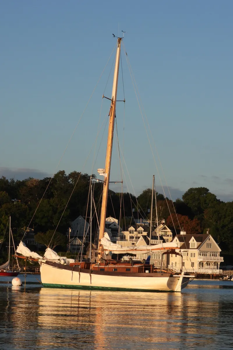 Slide: The Image of Sailboat "Lyle Hess Cutter" 1999, anchored near coastal homes at sunset. - 10