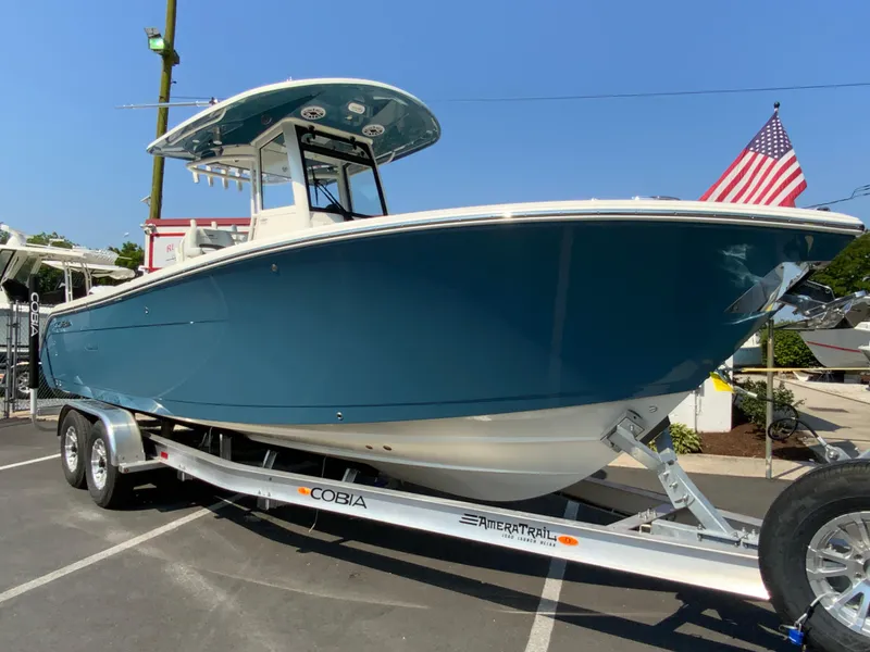 Slide: The Image of 2025 Cobia 265 CC boat on trailer, blue hull, American flag in background. - 2