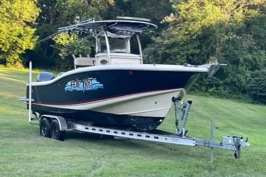 The Image of 2003 Scout 280 Sportfish boat on trailer, parked on grassy area with trees in background. - 0