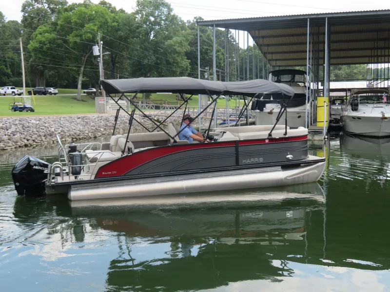 Slide: The Image of 2023 Harris Sunliner 230 pontoon boat docked at a marina with canopy and outboard motor. - 3