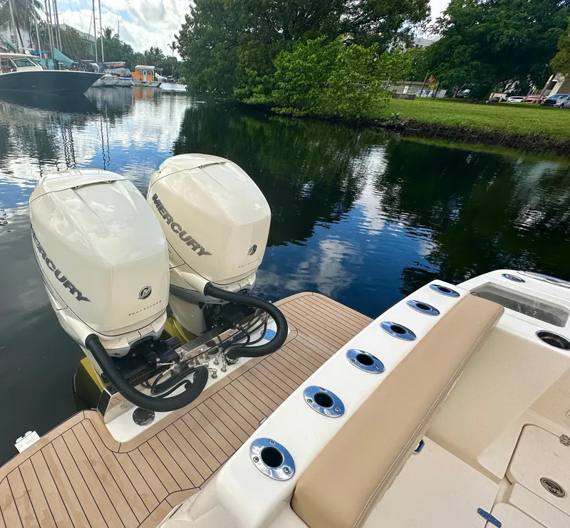 Slide: The Image of 2025 Scout 330 LXF boat with twin Mercury outboard engines docked by a serene waterway. - 2