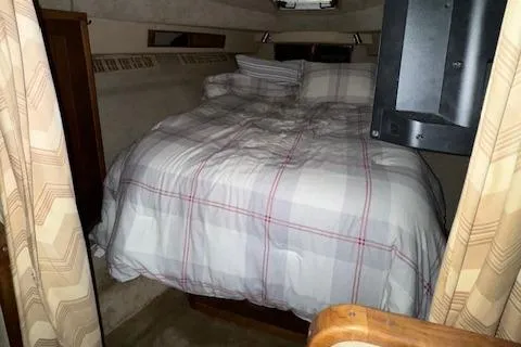 Slide: The Image of 1986 Sea Ray 340 Express Cruiser cabin with a cozy bed and plaid bedding. - 7