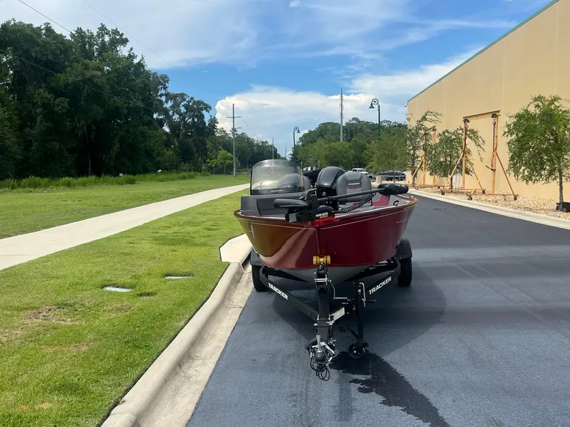Slide: The Image of 2024 Tracker Pro Guide V-16 SC boat parked on a paved road near greenery. - 3