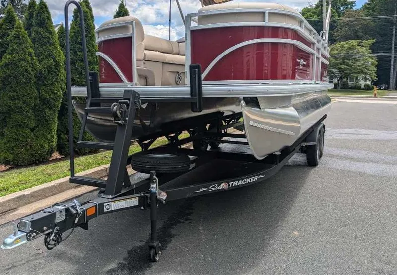 Slide: The Image of 2024 Sun Tracker Party Barge 20 DLX pontoon boat on trailer, red and silver, parked on street. - 2