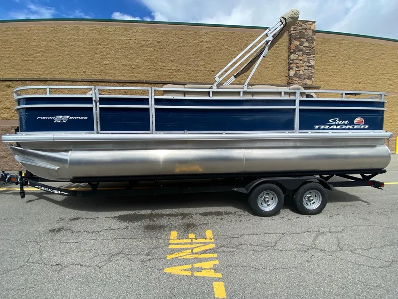 The Image of 2024 Sun Tracker Fishin' Barge 22 DLX pontoon boat on trailer, parked outdoors. - 0