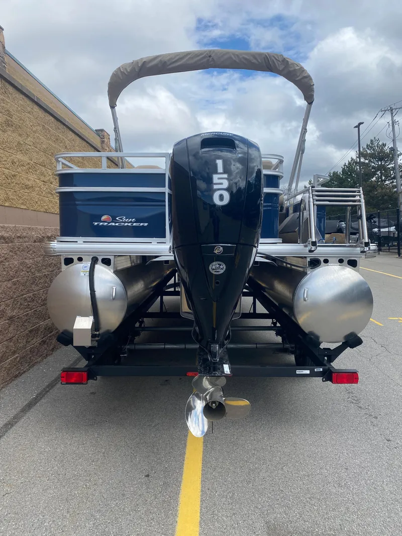 Slide: The Image of 2024 Sun Tracker Fishin' Barge 22 DLX pontoon boat with 150 HP engine, parked outdoors. - 2