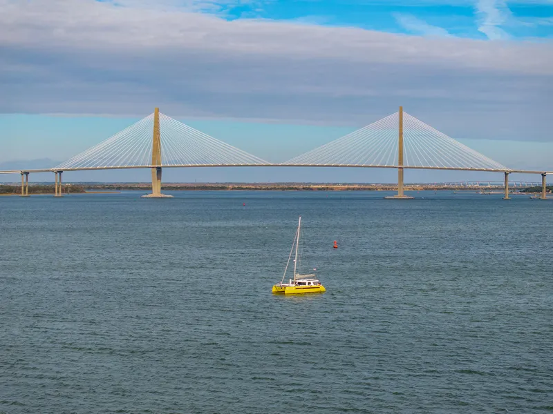 Slide: The Image of Yellow sailboat on water near a large suspension bridge under a blue sky. - 116