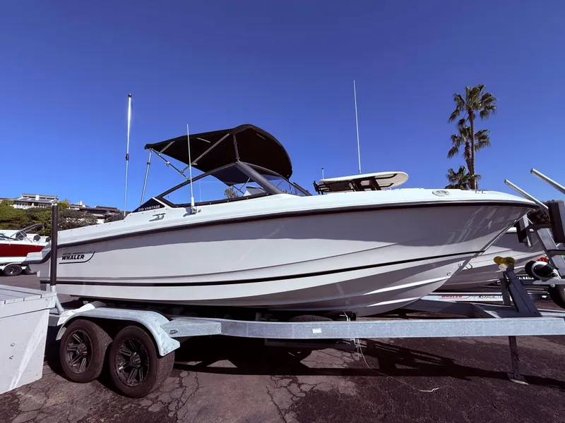 Slide: The Image of 2025 Boston Whaler 210 Vantage boat on trailer, parked outdoors under clear blue sky. - 2