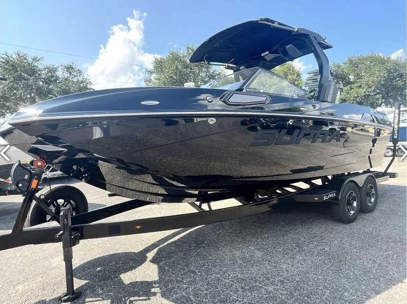 The Image of 2024 Supra SE 550 boat on trailer, sleek black design, sunny day. - 0