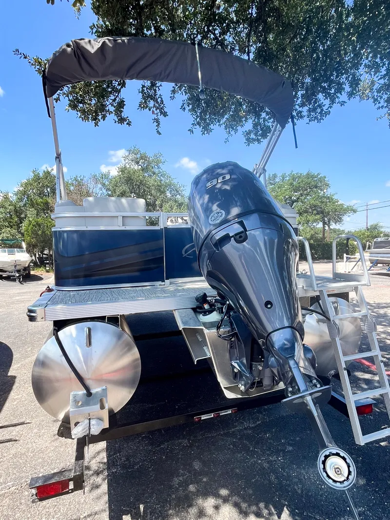 Slide: The Image of 2024 Avalon VLS 21 Quad Lounger boat with outboard motor and canopy, parked outdoors. - 3