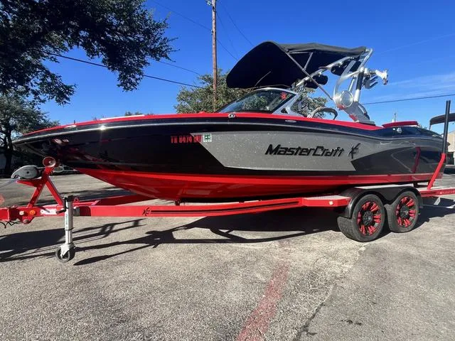 Slide: The Image of 2016 MasterCraft X30 boat on a red trailer, parked outdoors. - 2