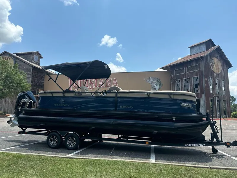 Slide: The Image of 2024 Regency 250 LE3 pontoon boat on trailer in parking lot. - 2