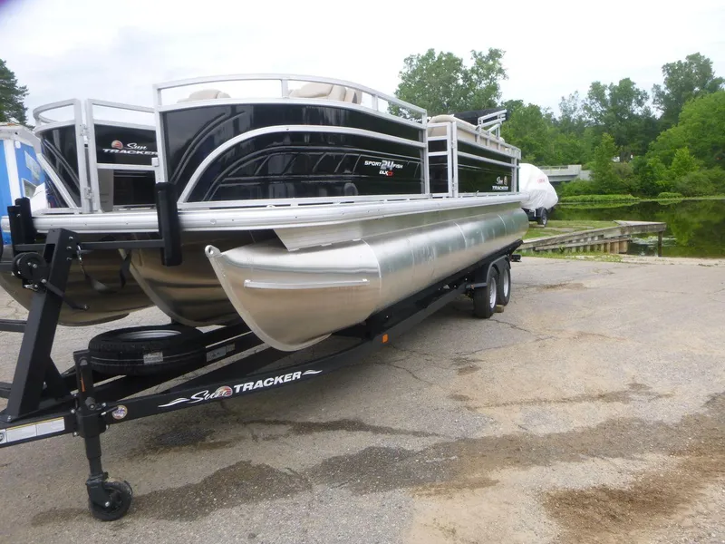 Slide: The Image of 2024 Sun Tracker Sportfish 24 XP3 pontoon boat on trailer by a lake. - 16
