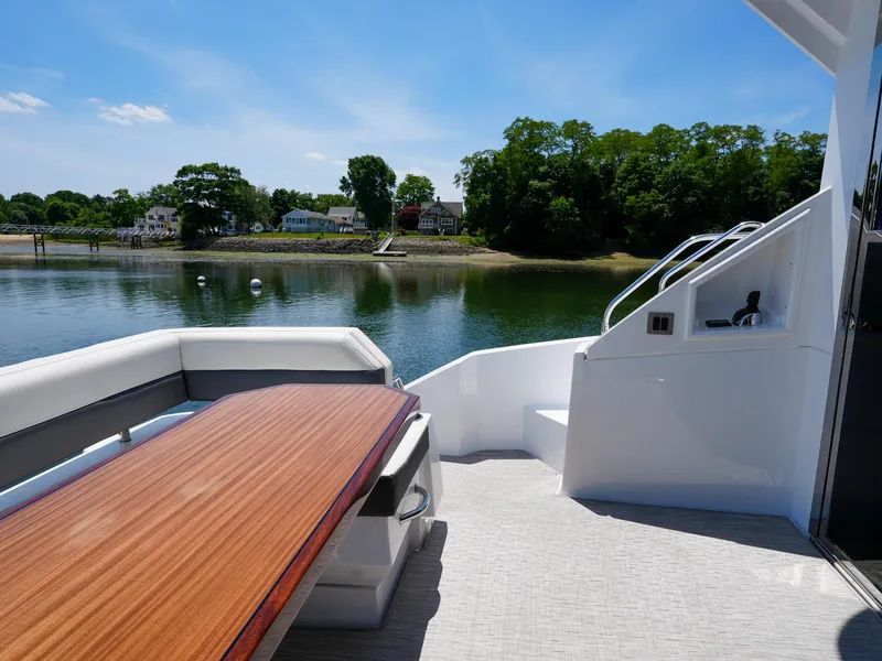 Slide: The Image of 2021 Cruisers Yachts 50 Cantius deck with wooden table, white seating, and scenic waterfront view. - 13