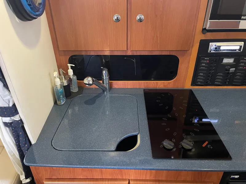 Slide: The Image of 2008 Bayliner 340 kitchen area with sink, stove, and wooden cabinets. - 25