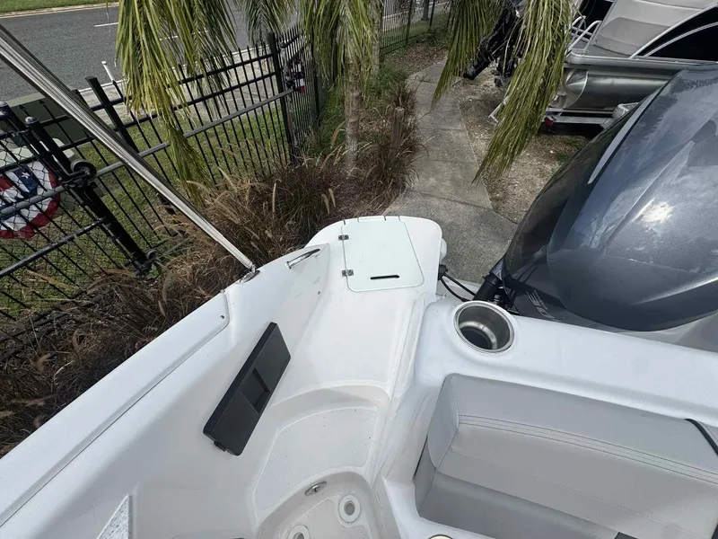 Slide: The Image of 2025 Hurricane SunDeck 2400 OB boat interior with seating and cup holder, near palm trees. - 7