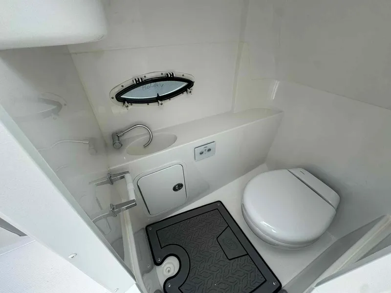 Slide: The Image of 2025 Hurricane SunDeck 2400 OB boat bathroom with sink, toilet, and porthole window. - 9