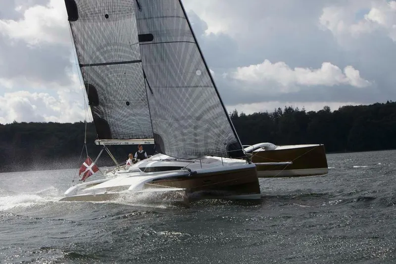 Slide: The Image of Sailing Dragonfly 32 trimaran on water, 2026 model, with Danish flag, under cloudy sky. - 2