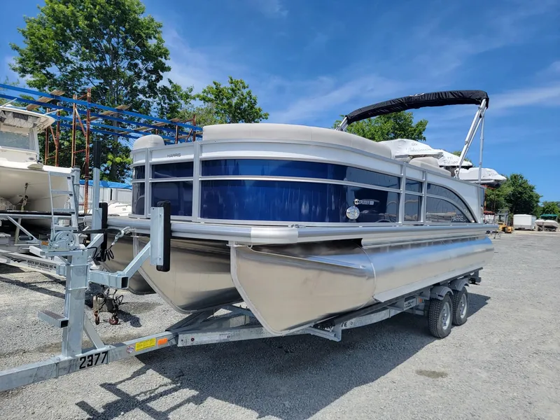 Slide: The Image of 2025 Harris Cruiser 210 pontoon boat on a trailer, parked outdoors. - 0
