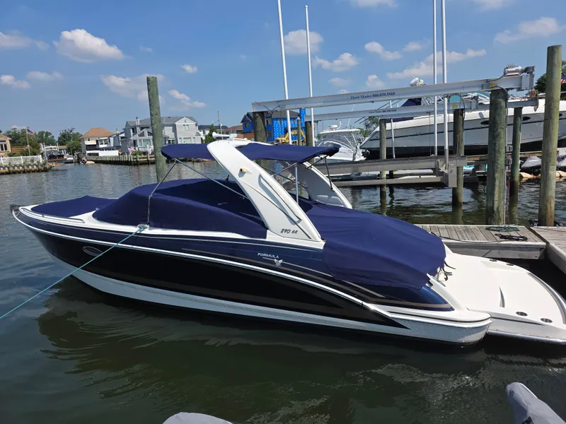 Slide: The Image of A 2015 Formula Bowrider 290 docked. It features a blue cover and white detailing. - 0