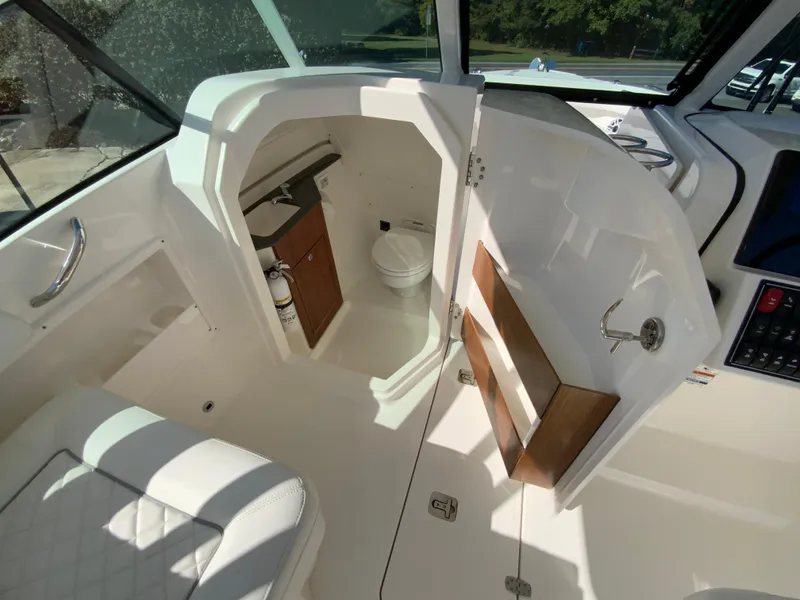 Slide: The Image of 2025 Pursuit DC 246 Dual Console boat interior with open door to compact bathroom. - 20