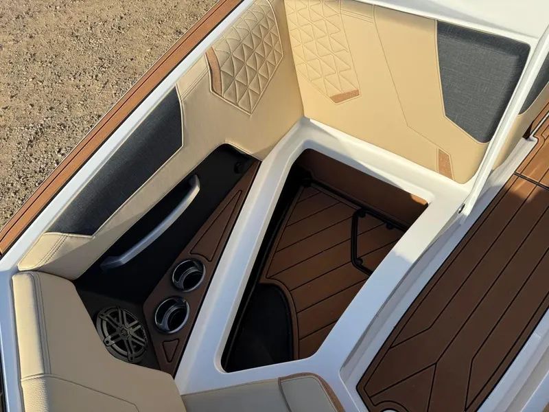 Slide: The Image of 2025 Nautique Super Air GS22 boat interior with tan and gray seating, cup holders, and speaker. - 17