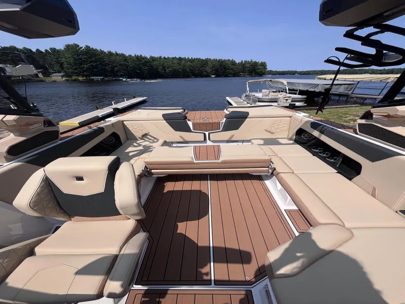 Slide: The Image of 2025 Nautique Super Air GS22 boat interior with tan seating and wood flooring by a lake. - 20