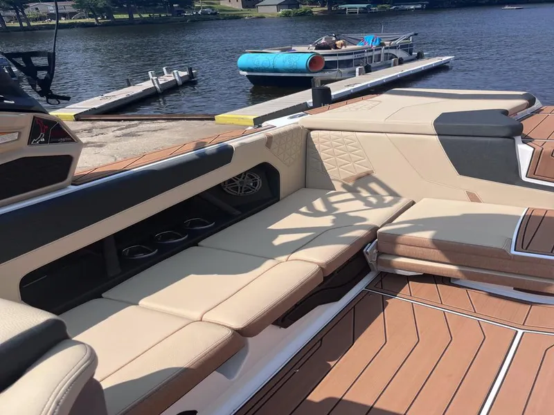 Slide: The Image of 2025 Nautique Super Air GS22 boat interior with tan seating by a lake. - 26
